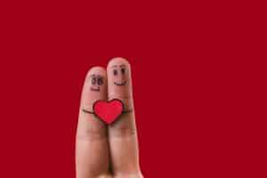 zwei zusammengepresste Finger mit gezeichneten Strichen und Gesichtern, die sich umarmen und ein rotes Herz halten