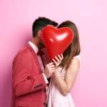 Küssendes Paar hinter einem roten herzförmigen Ballon